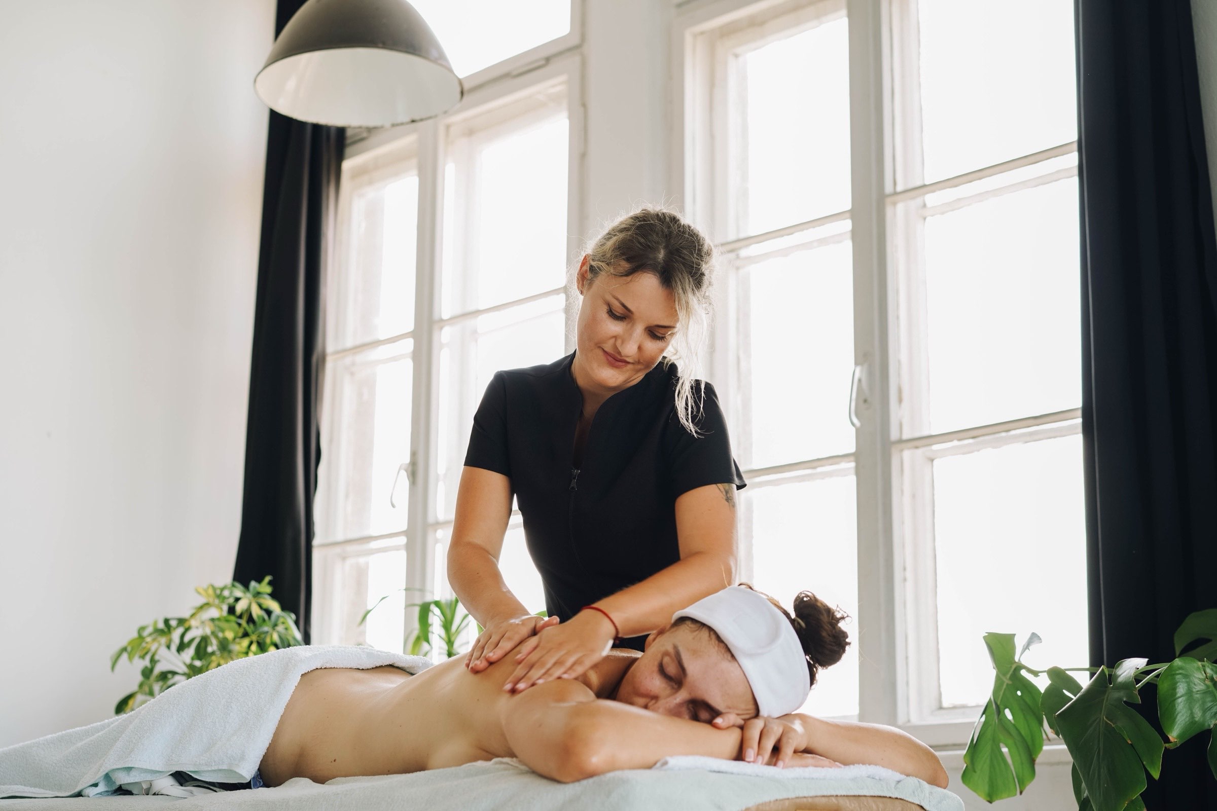 Person som får en lugn massagebehandling i ett ljust rum med stora fönster och gröna växter